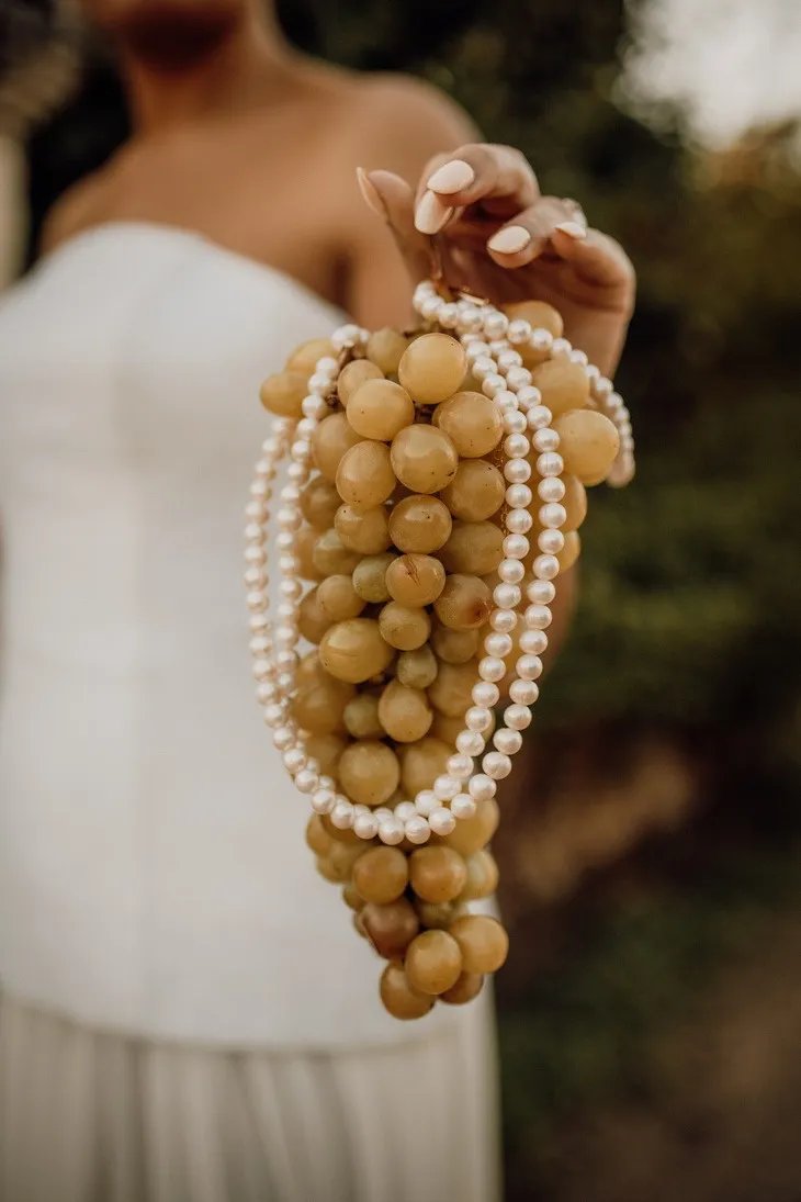 Une mariée tient une grappe de raisin enroulée d'un collier de perles